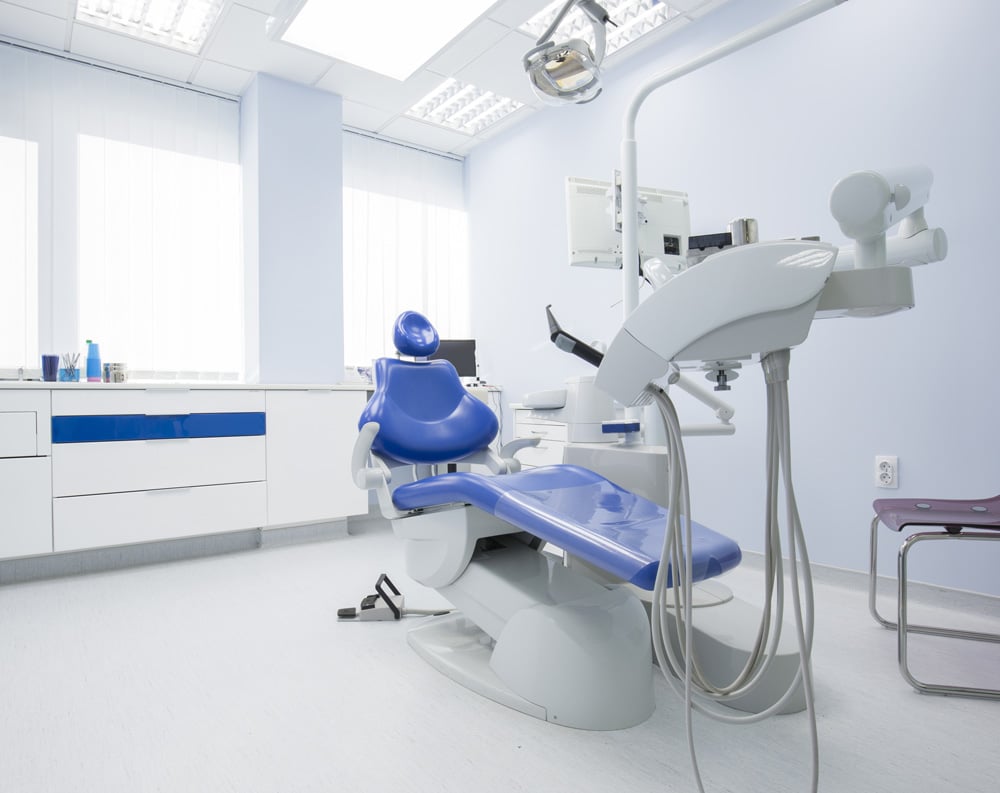 Modern dental clinic in Raleigh with a central dental chair surrounded by advanced dental equipment, including a dental light, instrument trays, monitors, and cabinets, in a clean and professional setting